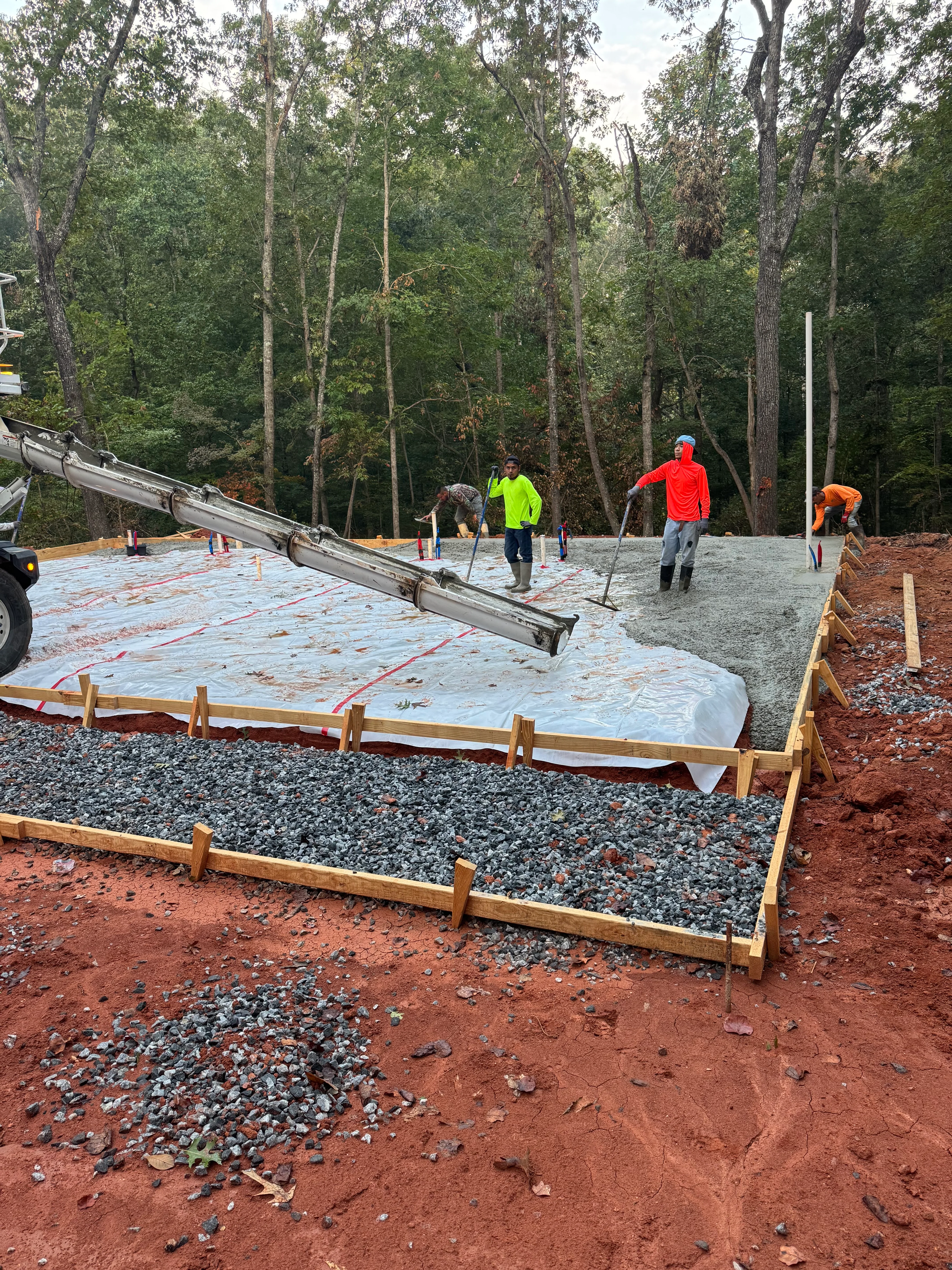 Gravel base and vapor barrier foundation prep with wooden frame borders and crew workers
