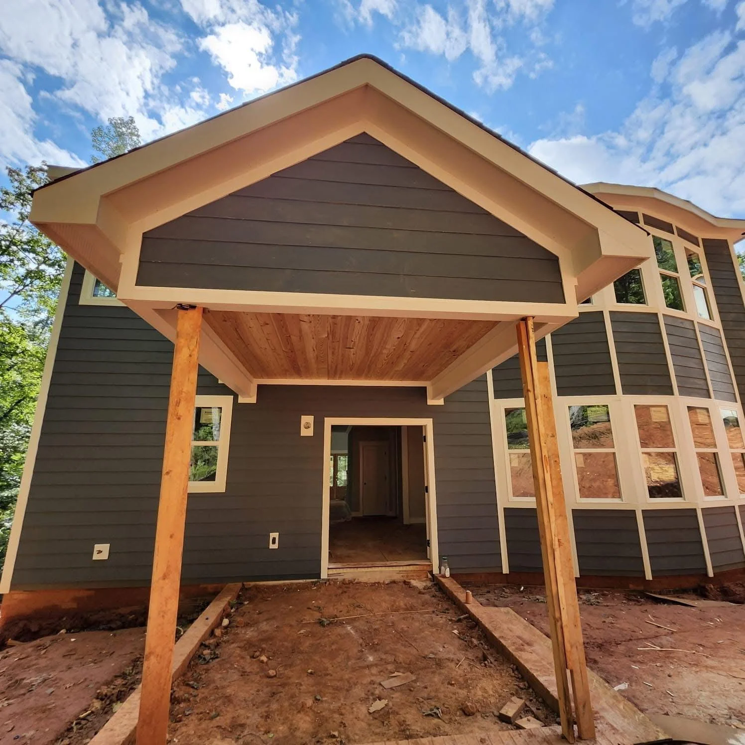 Modern home addition with timber posts, dark siding, and geometric covered entry portico
