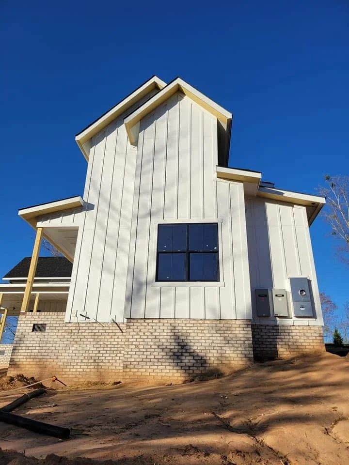 Standing seam metal roof with wood trim, white vertical siding, and brick foundation on modern home