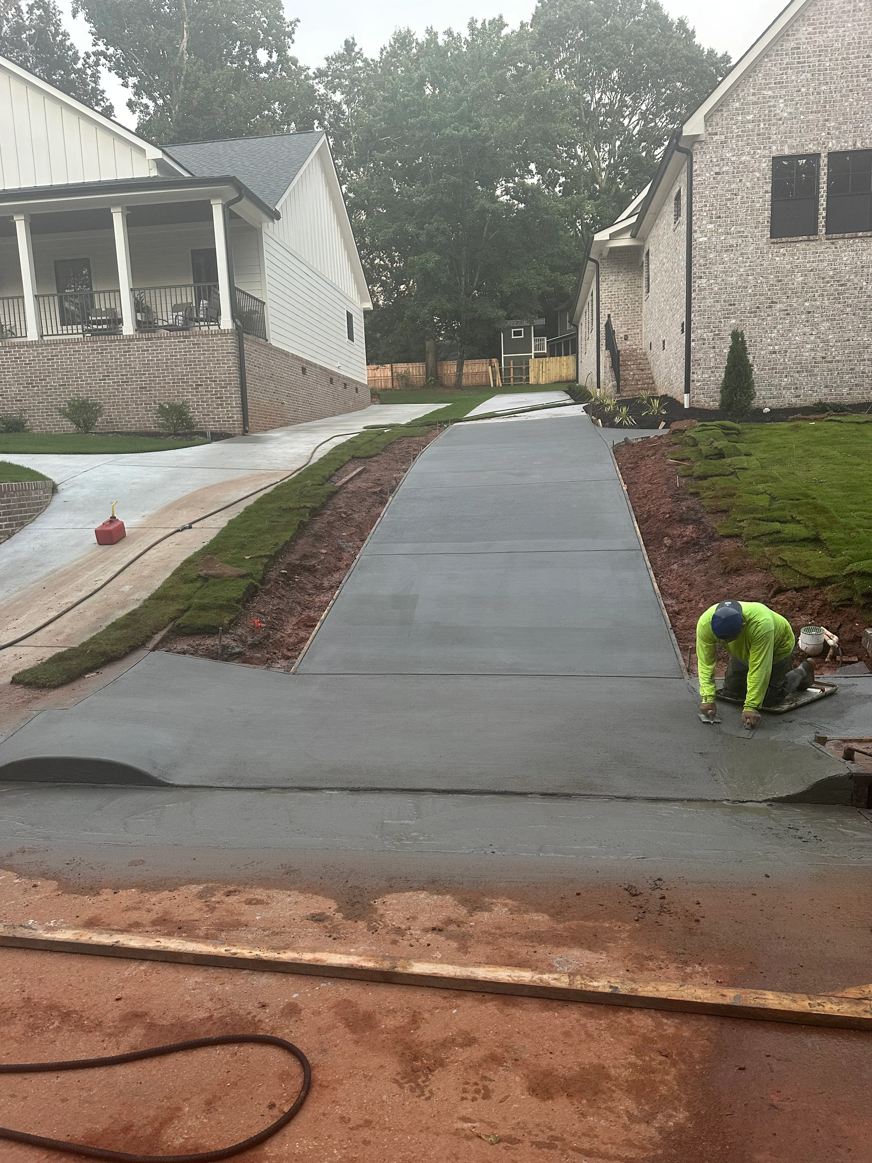 Concrete driveway installation in progress with finished concrete pad and landscaping work
