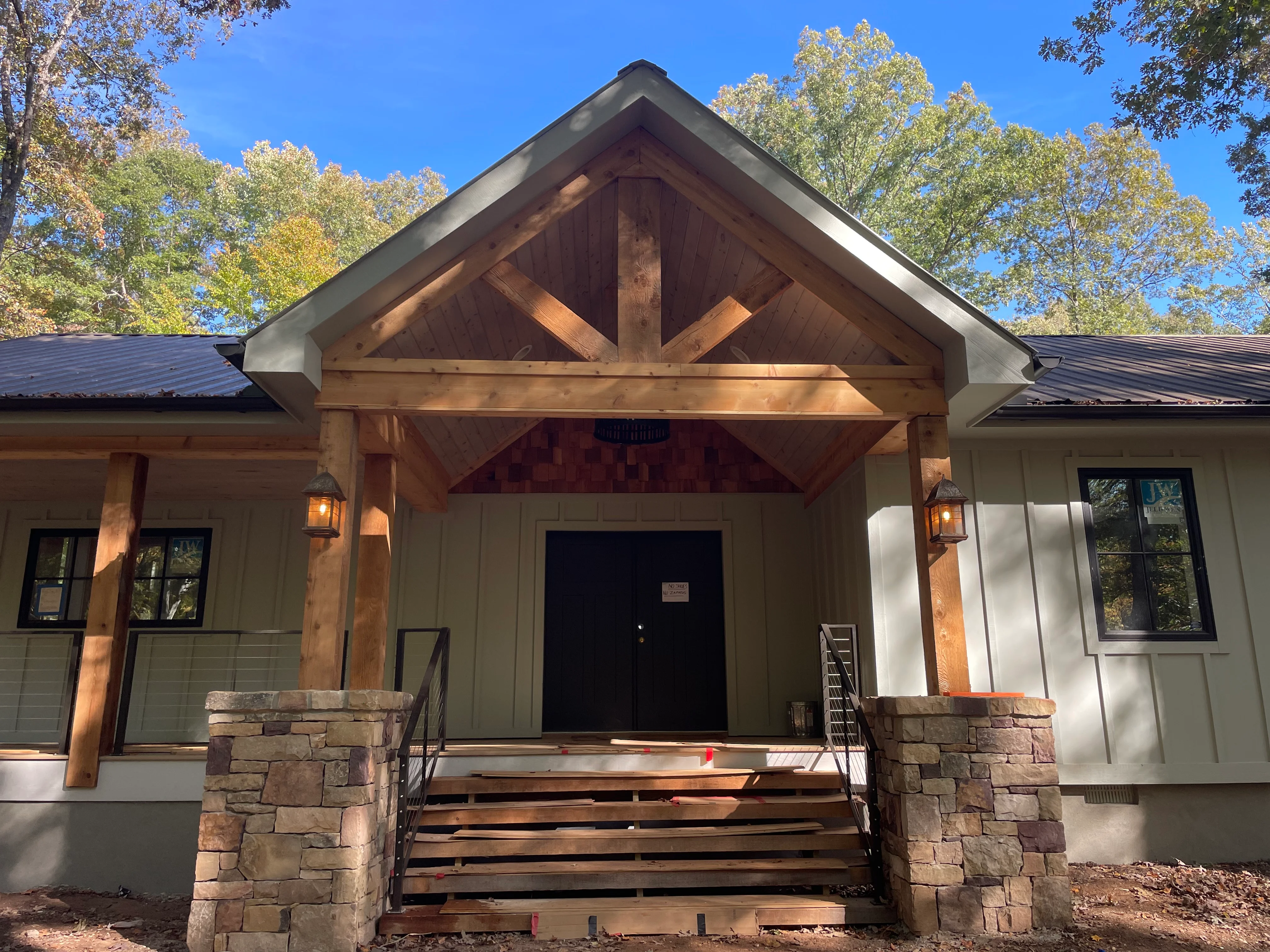 Standing seam metal roof with gabled entry, exposed timber beams, and stone veneer pillars