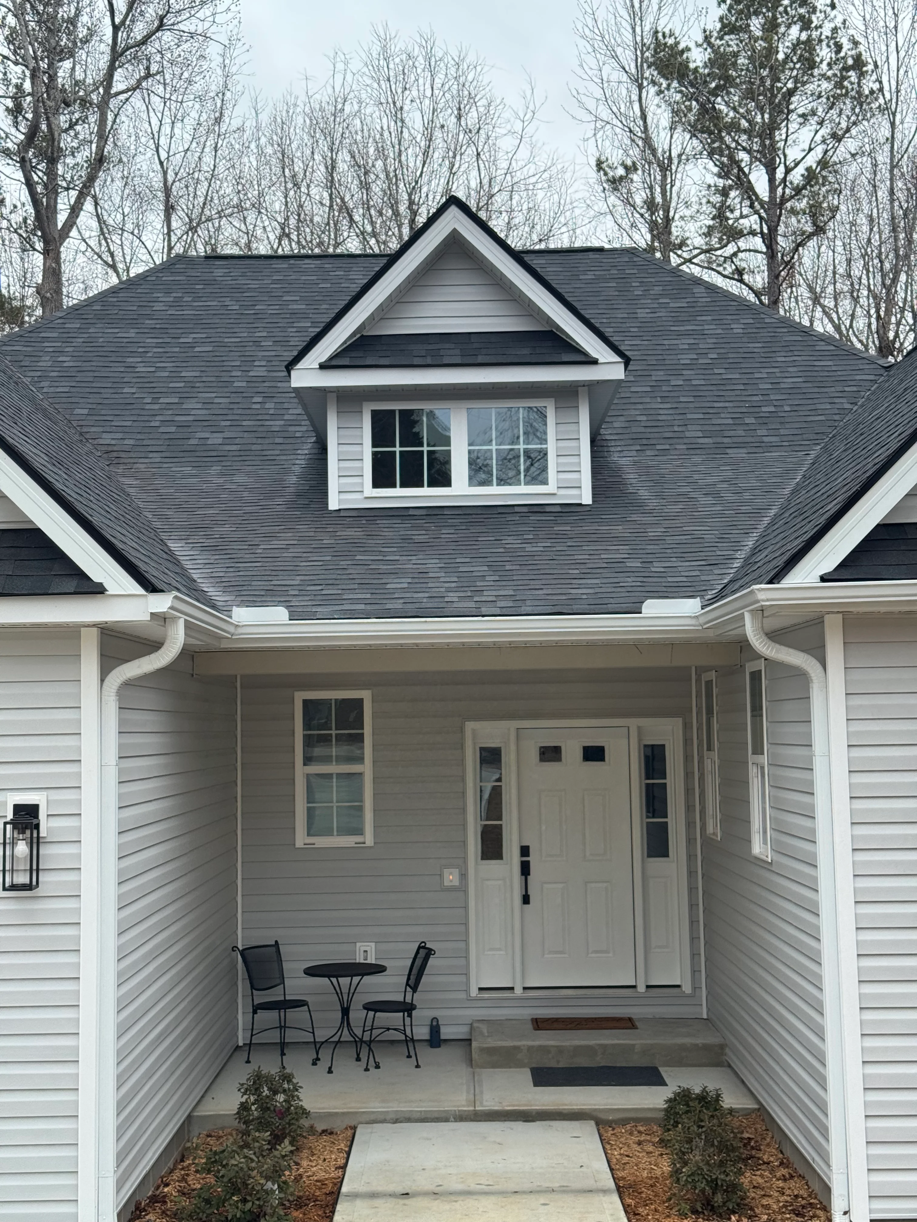 New charcoal gray architectural shingle roof with white dormer and fascia trim on residential home