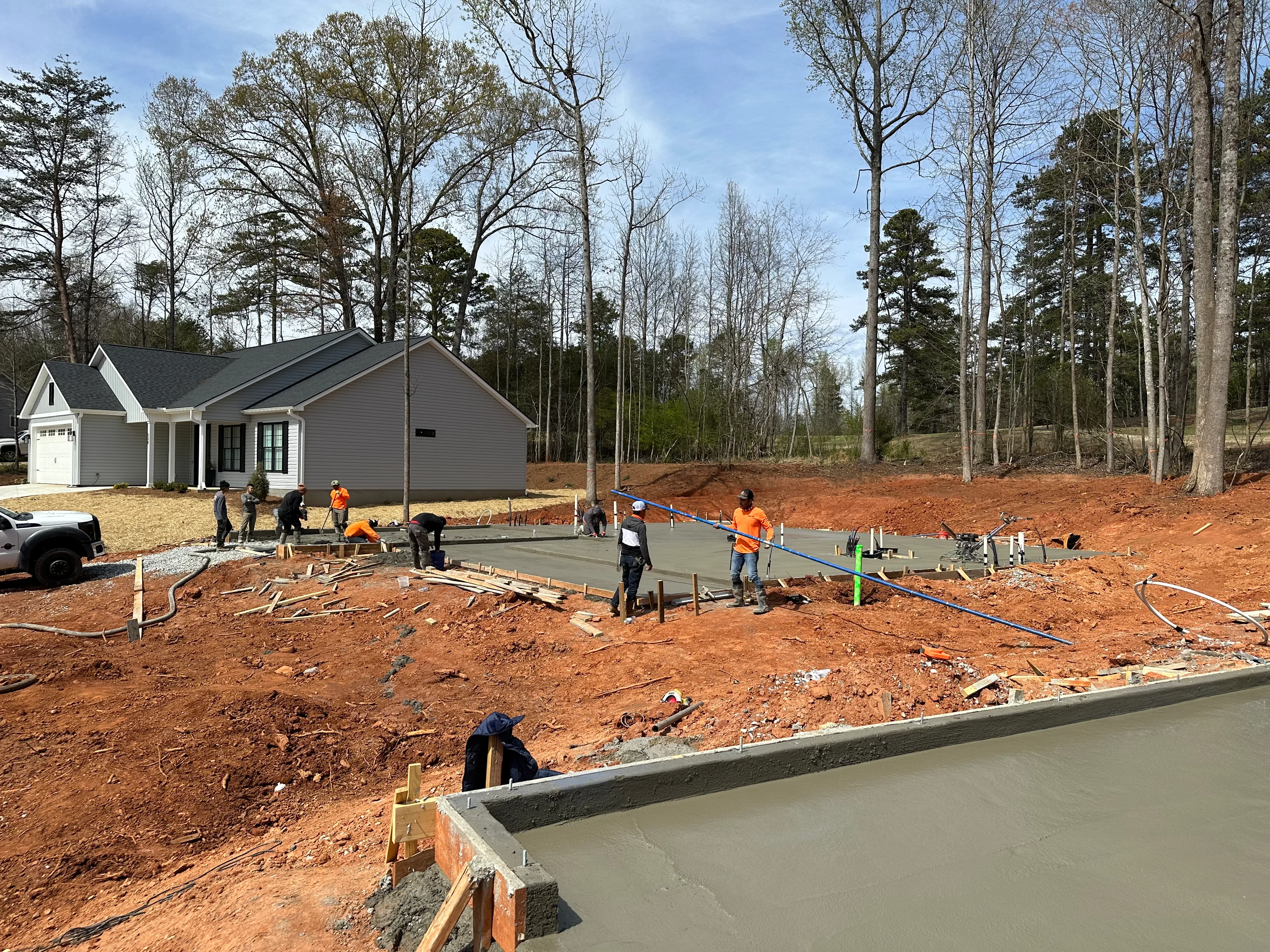 Concrete foundation pour in progress with crew finishing concrete slab on prepared red clay lot
