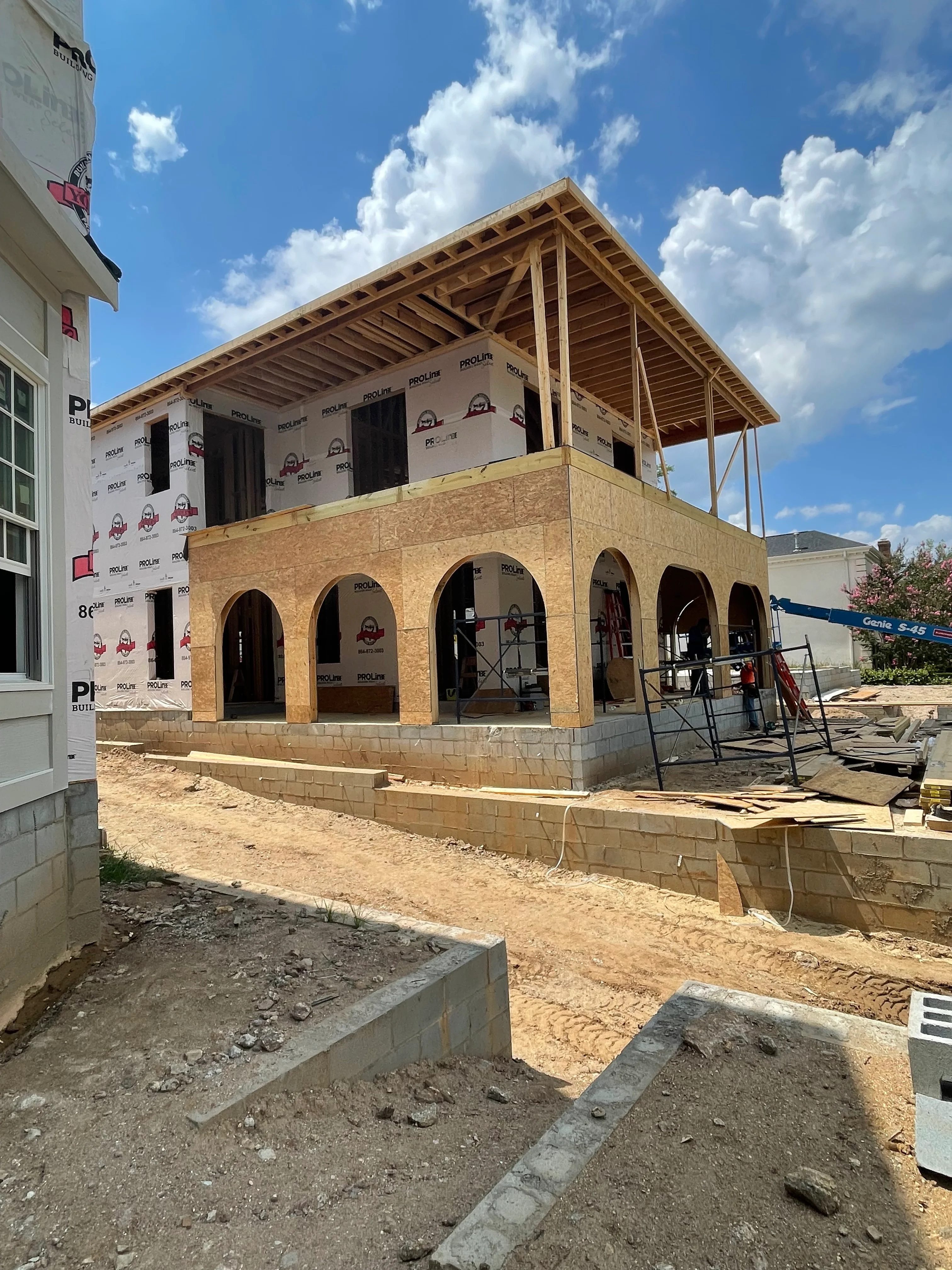 Two-story home under construction with brick arches, wood framing, and gable roof structure