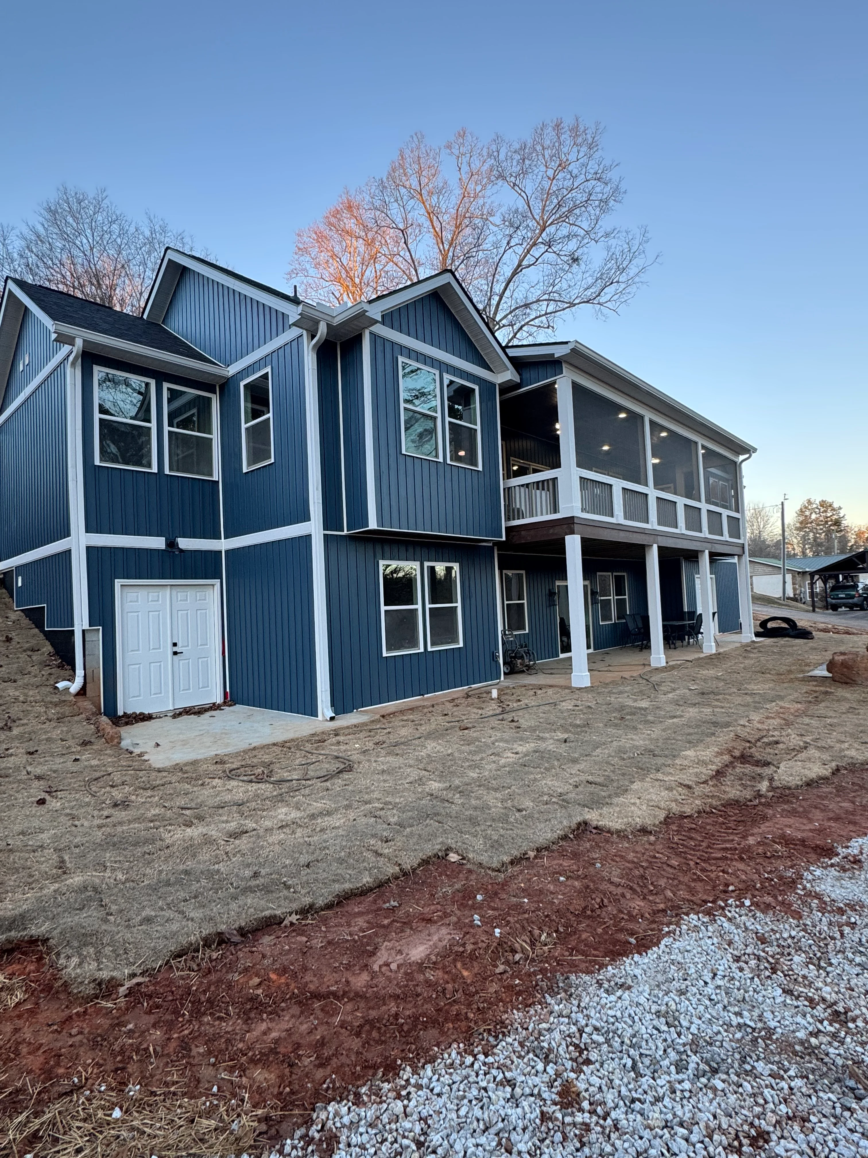 Two-story home with standing seam metal roof, navy vertical siding, white trim, and screened porch