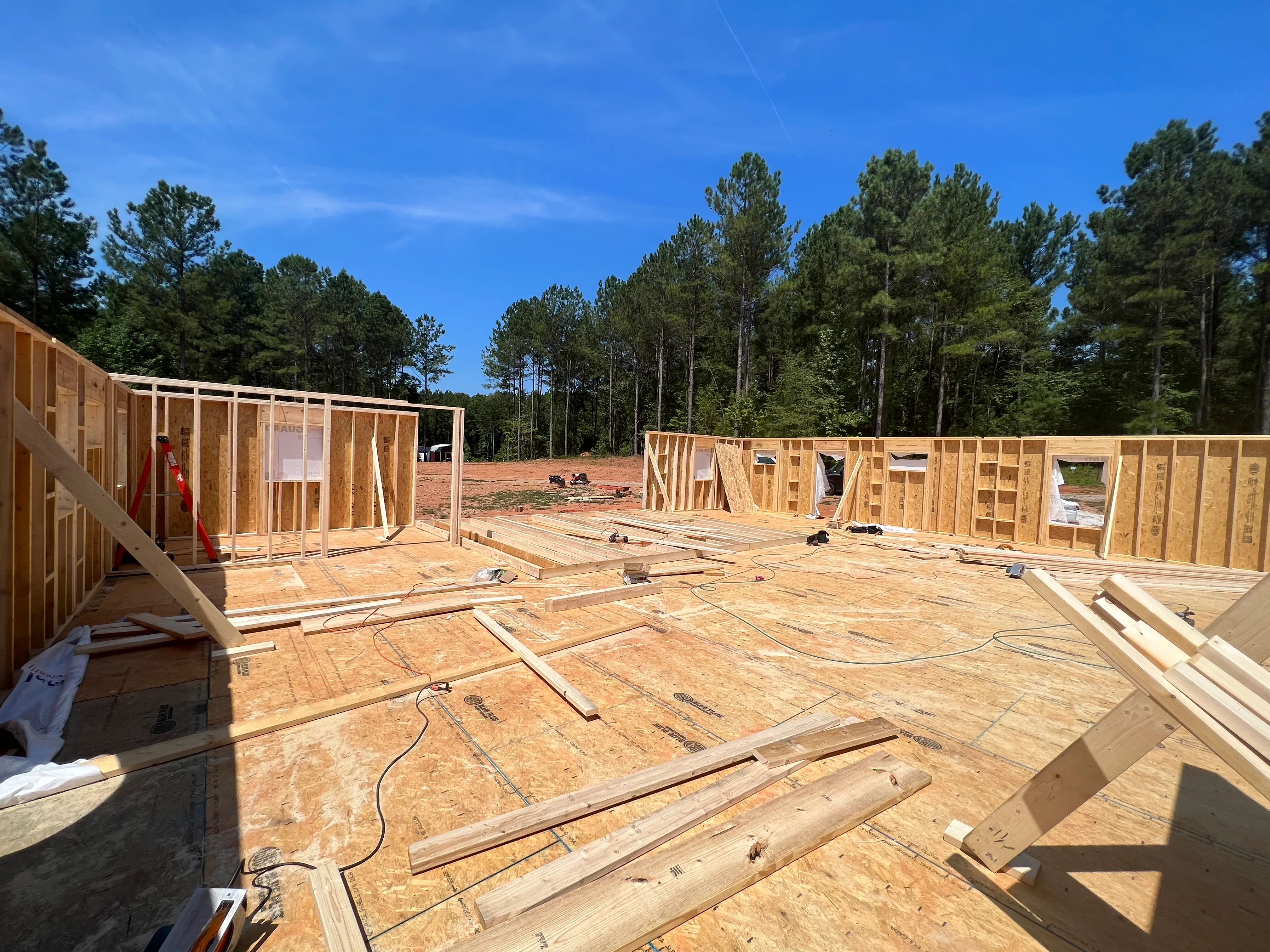 Residential framing construction with lumber walls, OSB flooring, and window openings on cleared lot